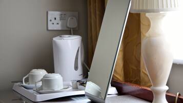 A hotel room with a coffee maker, a tray with cups and saucers, a lamp, and a window with curtains.