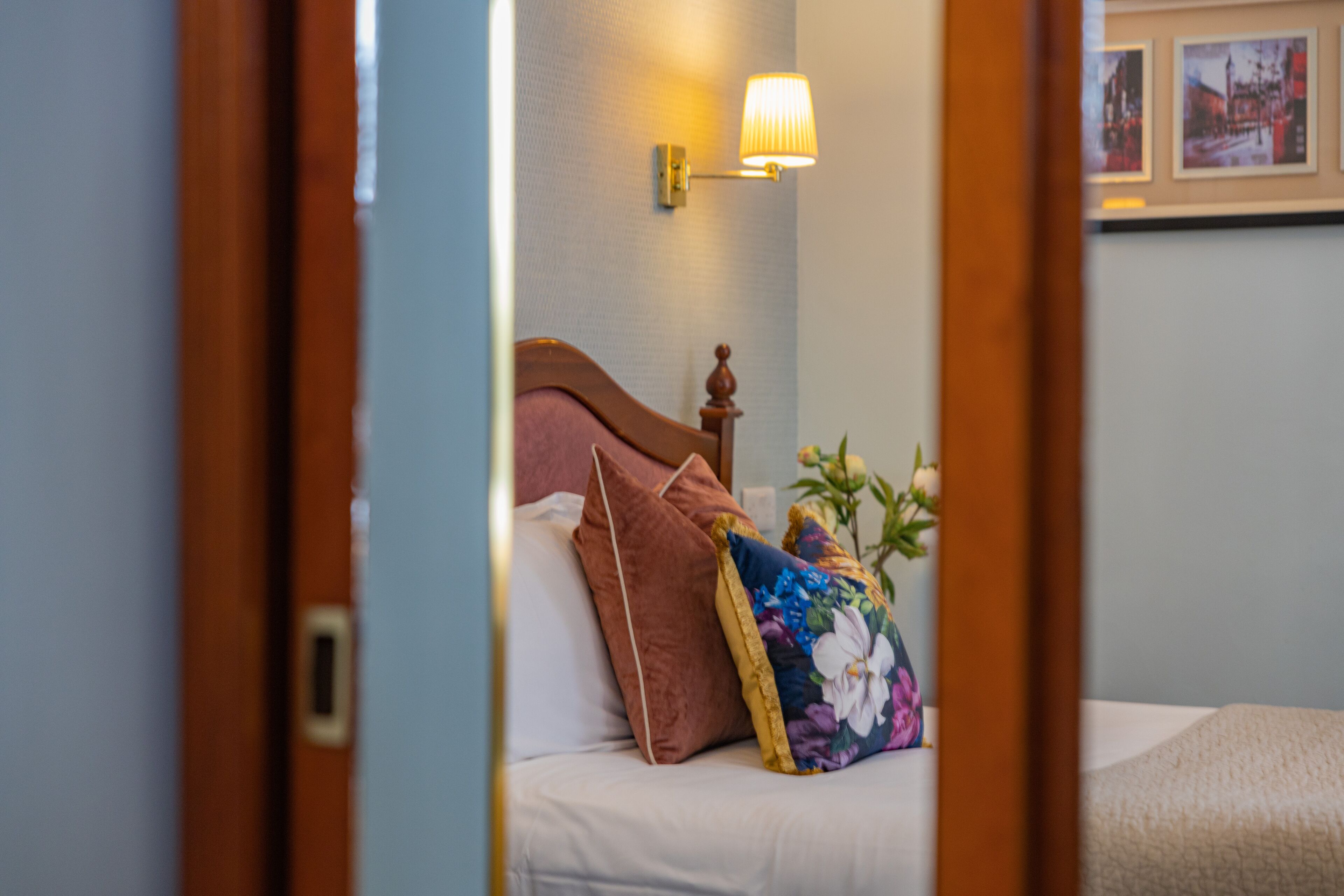 A bedroom with a bed, pillows, a nightstand, a lamp, and a wall-mounted picture.