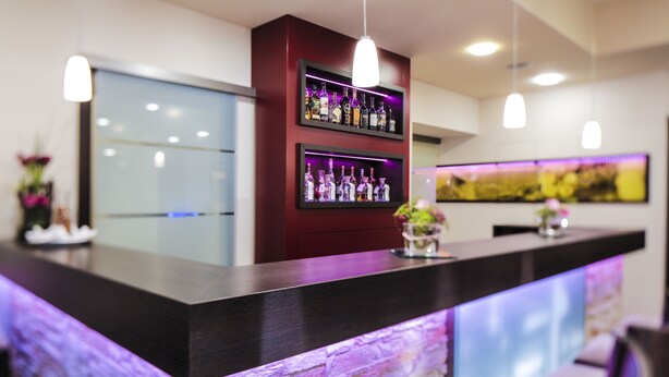 Una zona de bar con un mostrador oscuro, estanterías llenas de botellas e iluminación colgante.