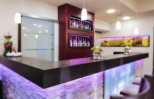 Una zona de bar con un mostrador oscuro, estanterías llenas de botellas e iluminación colgante.
