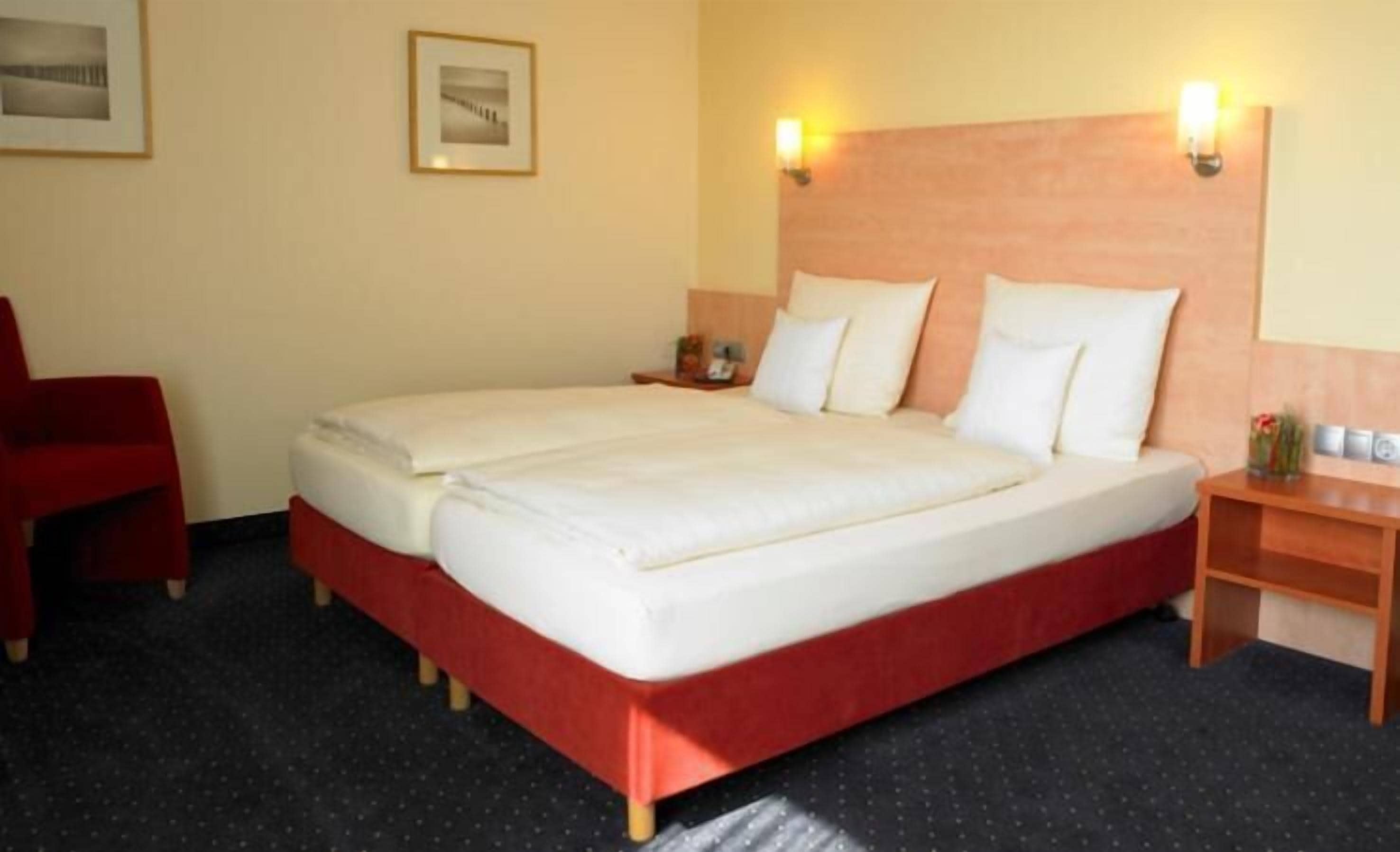 A hotel room with a double bed, two bedside tables, a red chair, and a framed picture on the wall.
