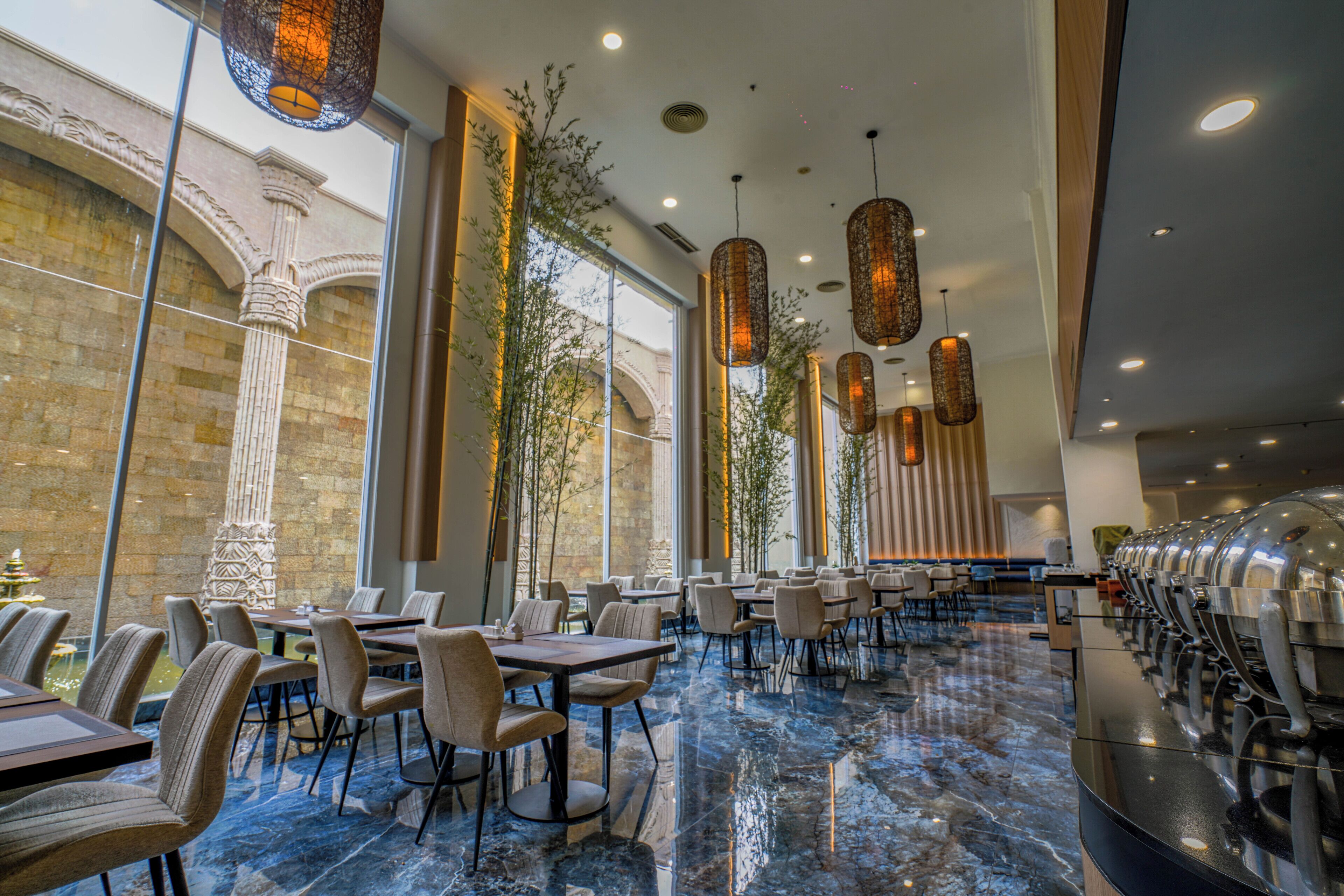 A spacious restaurant with marble flooring, multiple dining tables, and hanging pendant lights.