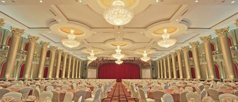 A banquet hall with rows of round tables, white chairs, and chandeliers.