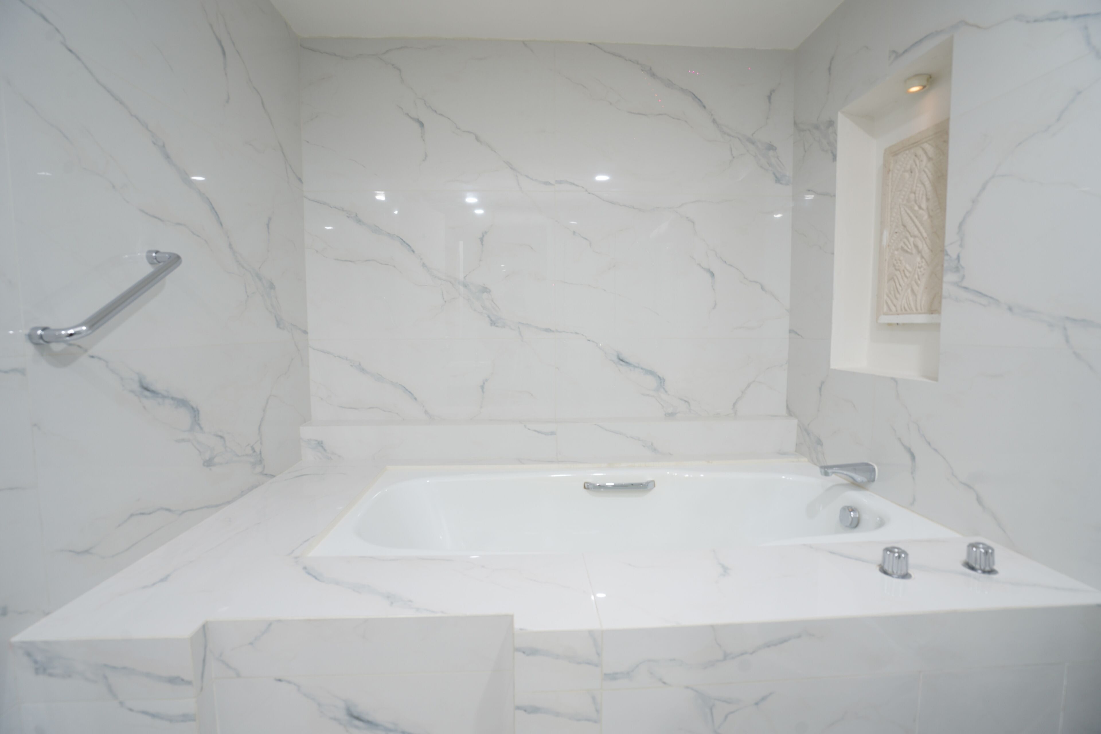 A bathroom with a marble wall, a bathtub, and a handrail.
