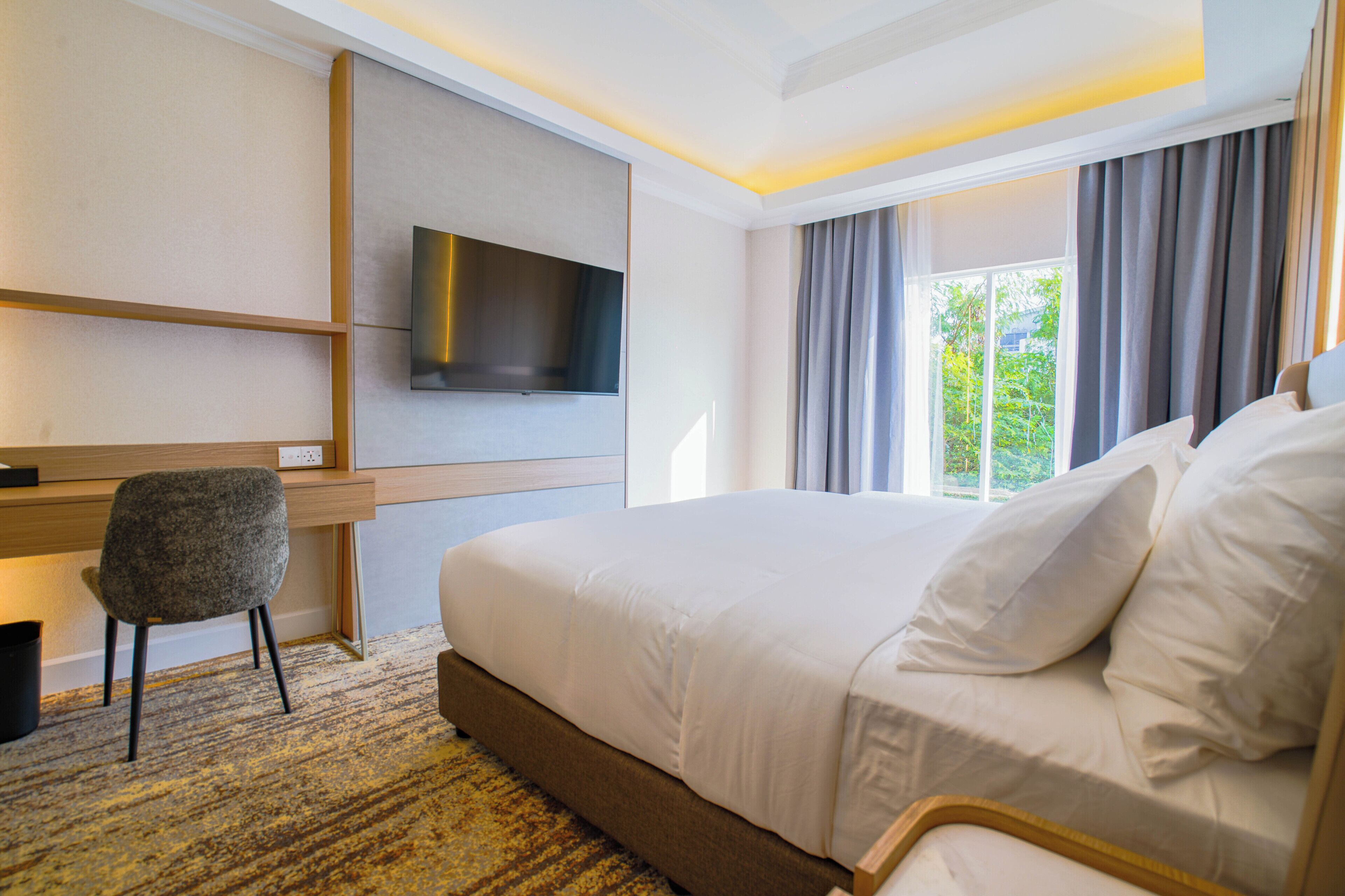 A hotel room with a bed, a desk, a chair, a flat-screen TV, and a window with curtains.