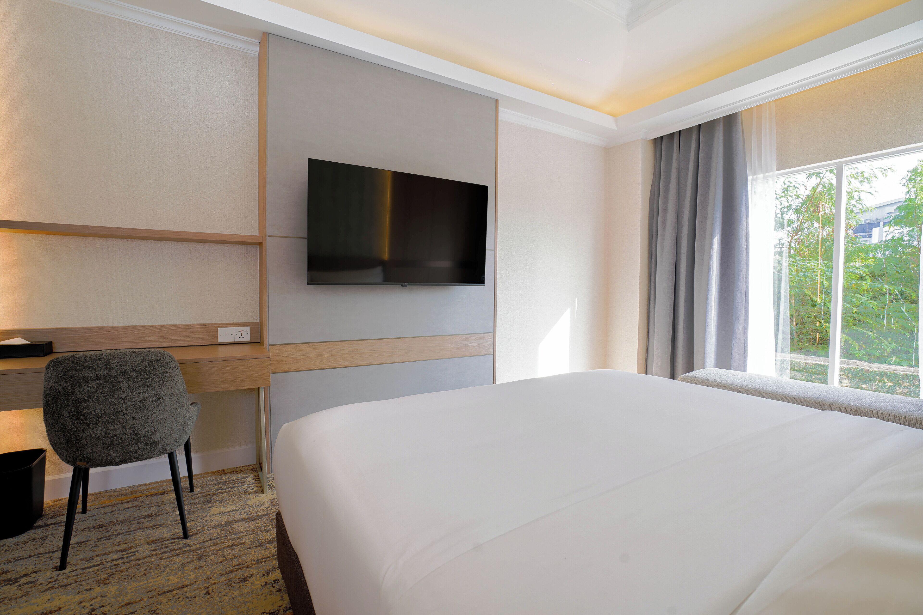 A hotel room with a bed, a desk, a chair, a television, and a window with curtains.