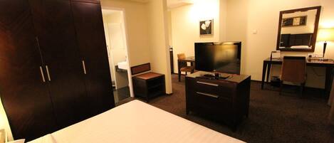 Una habitación de hotel con una cama grande, un escritorio con una silla, un televisor y un armario.
