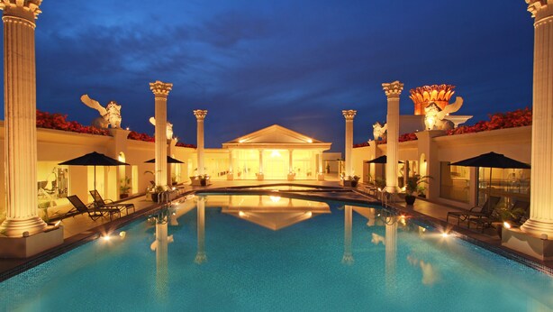 A large indoor swimming pool with columns and lounge chairs, surrounded by a building with classical architecture. - Harmoni One Convention Hotel & Service Apartments (Batam)