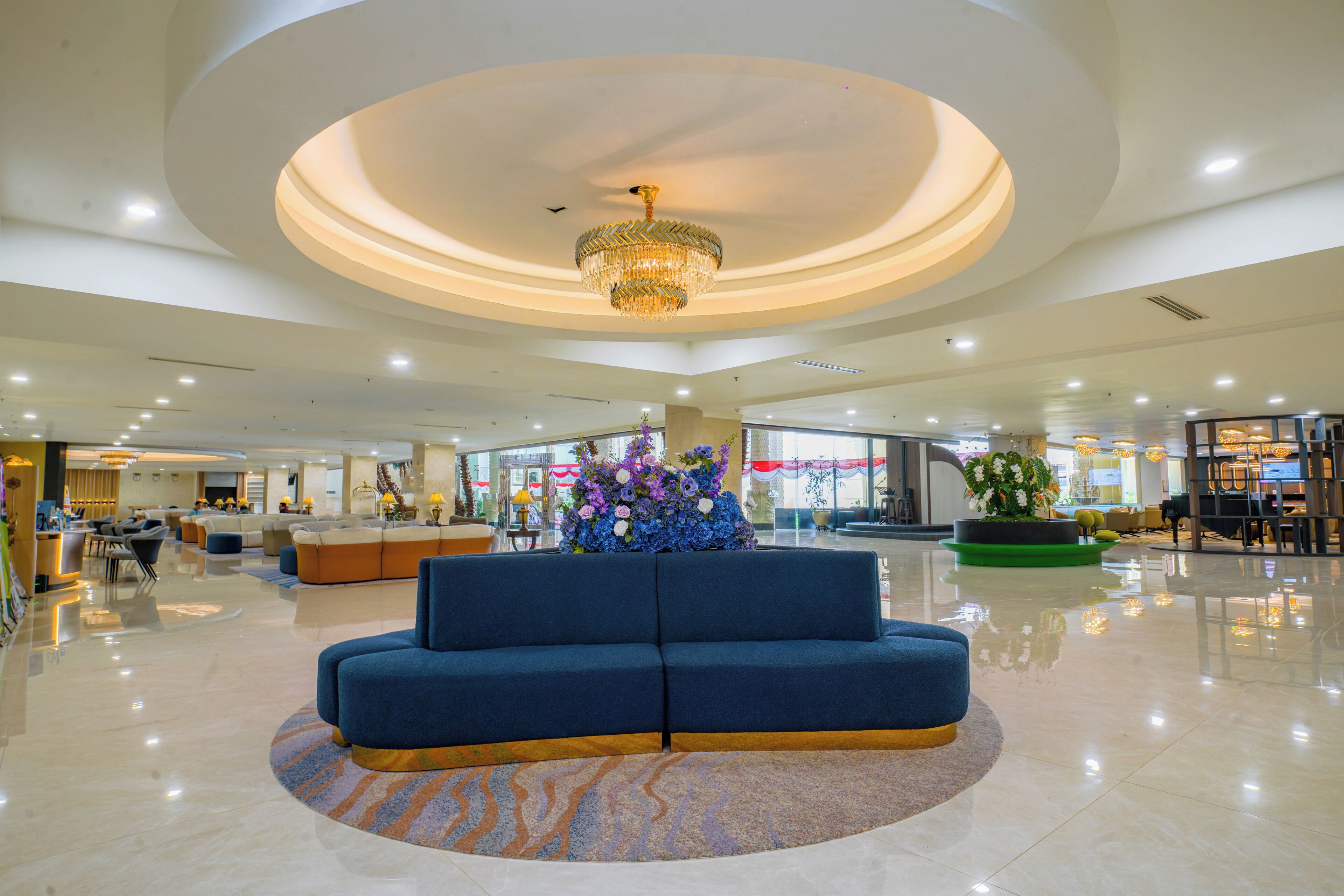 A spacious lobby with a central seating area, a chandelier, and a large window providing a view of the outside.