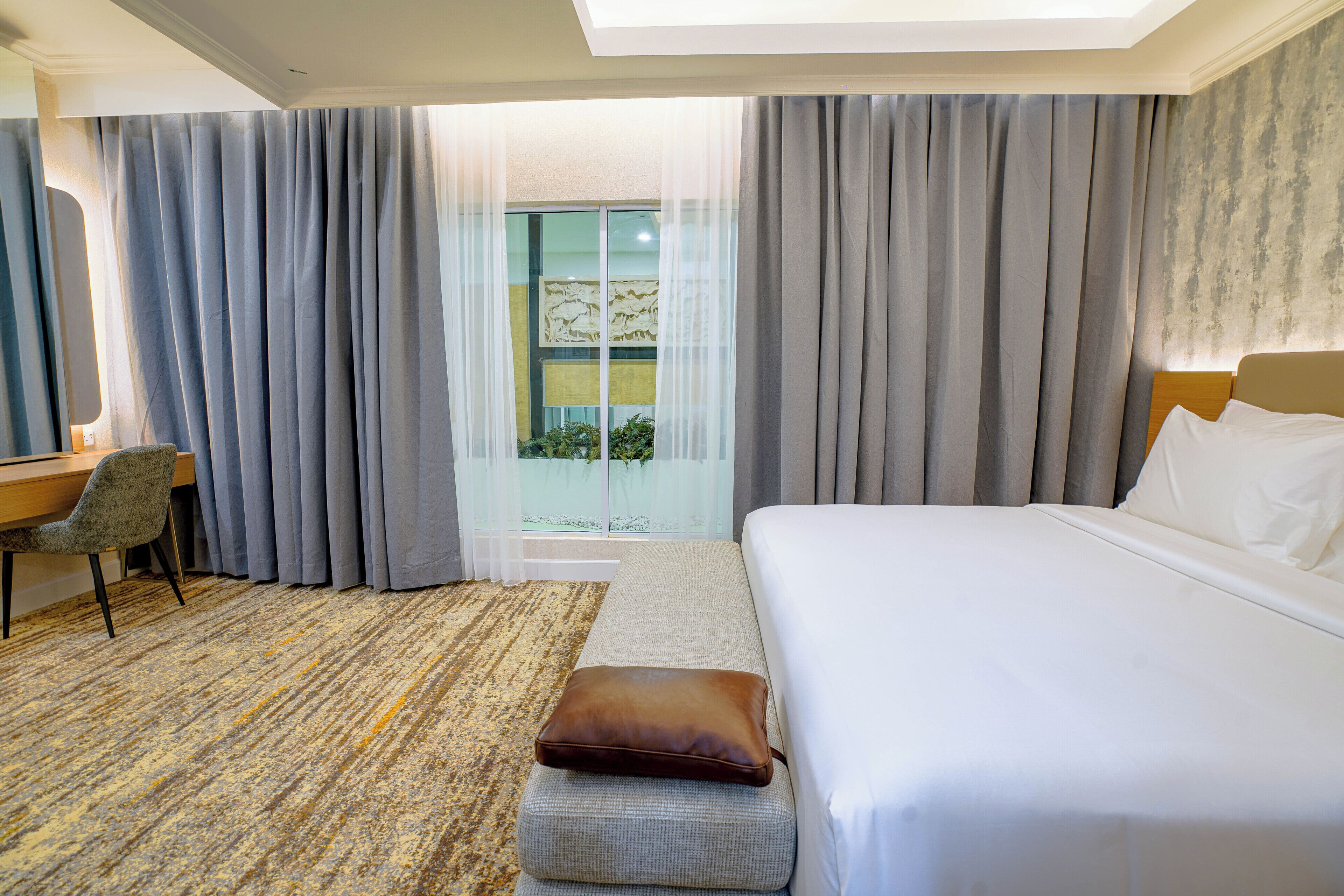 Ein Hotelzimmer mit Bett, Schreibtisch, Stuhl und Blick ins Freie.