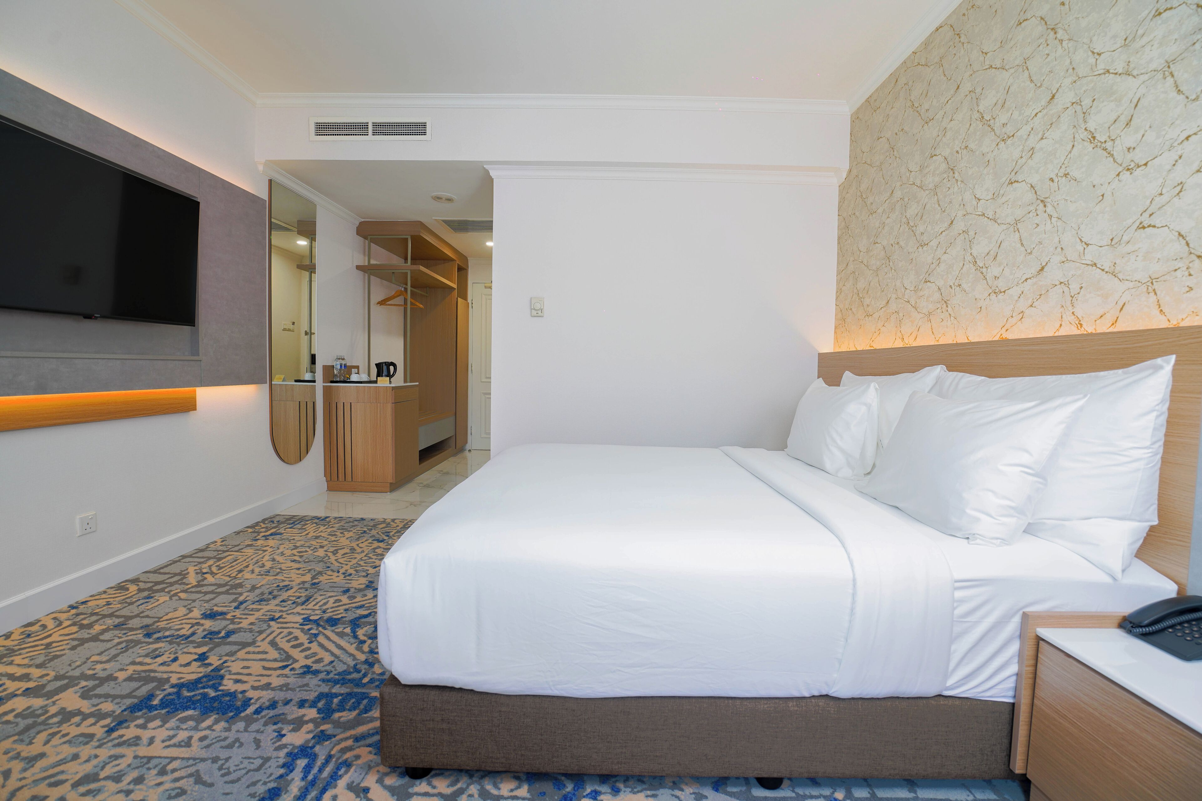 A hotel room with a bed, a bedside table, a TV, a wardrobe, and a bathroom visible through an open door.