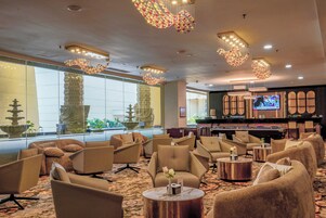 A hotel lobby with multiple seating areas, a bar, and a television screen.