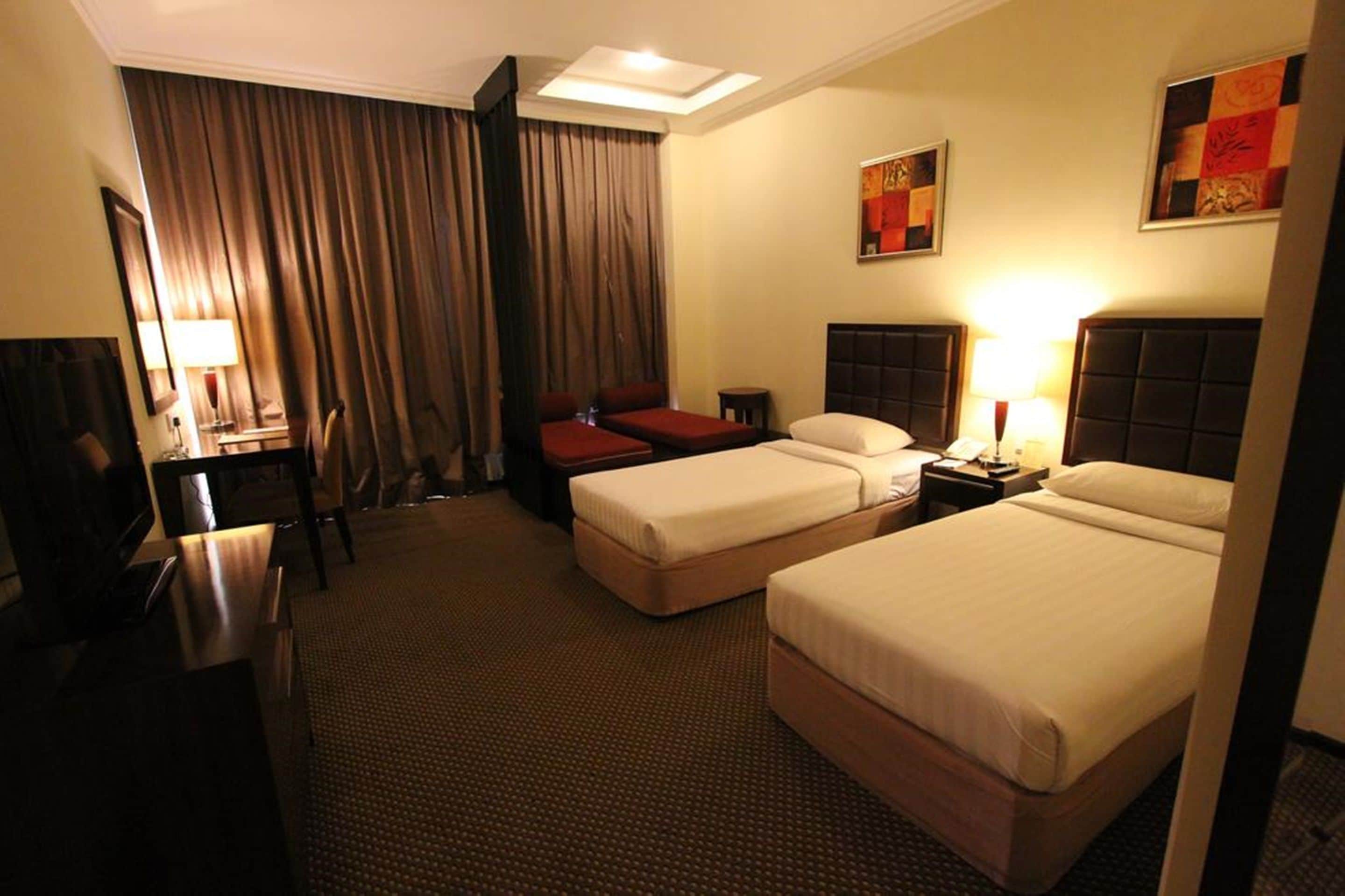 A hotel room with two beds, a desk, a chair, a TV, and a large window with curtains.