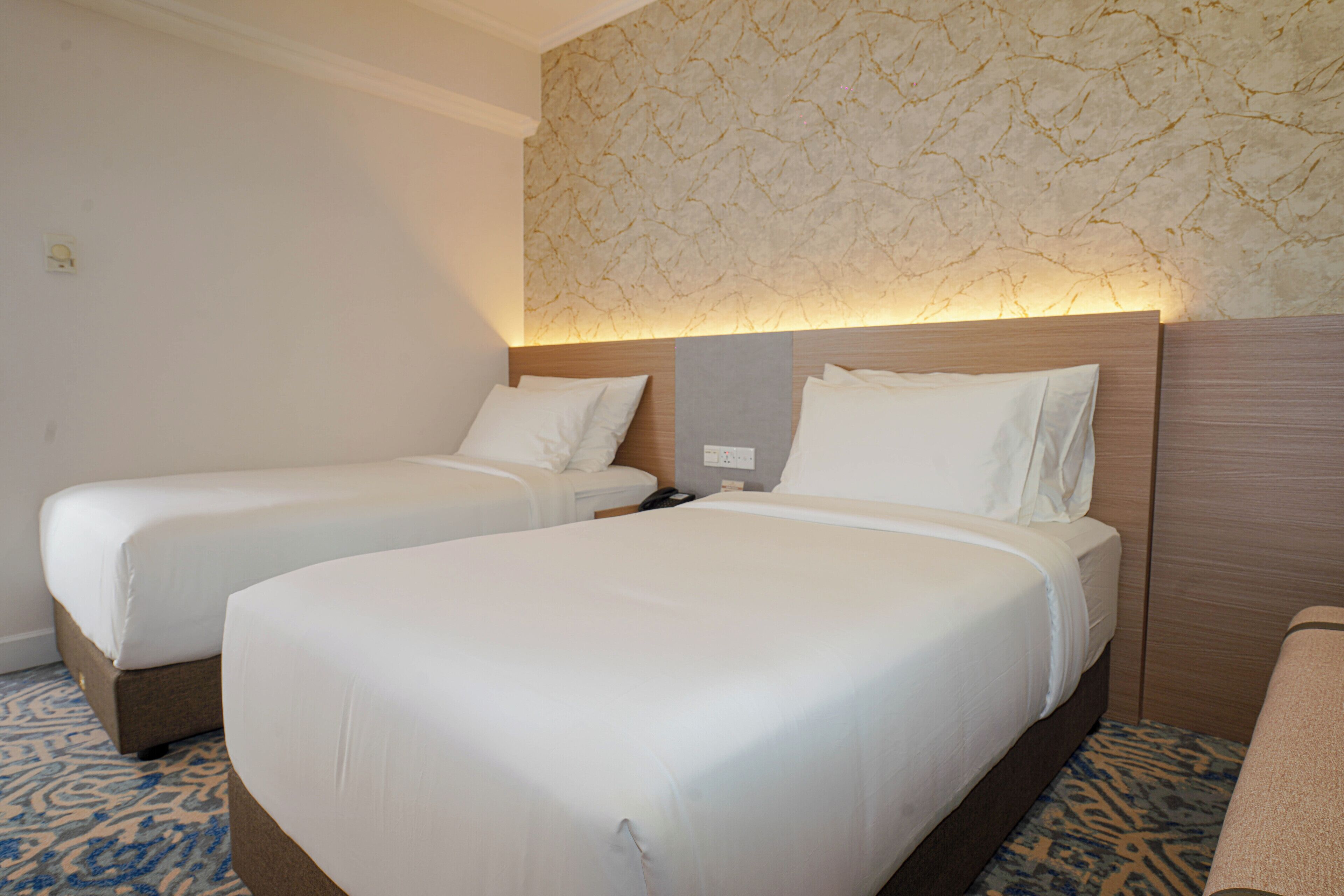 A hotel room with two single beds, a wooden headboard, and a patterned wall.