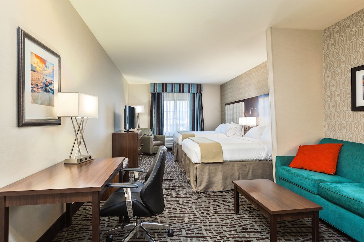 A hotel room with a desk, chair, bed, and a teal sofa.