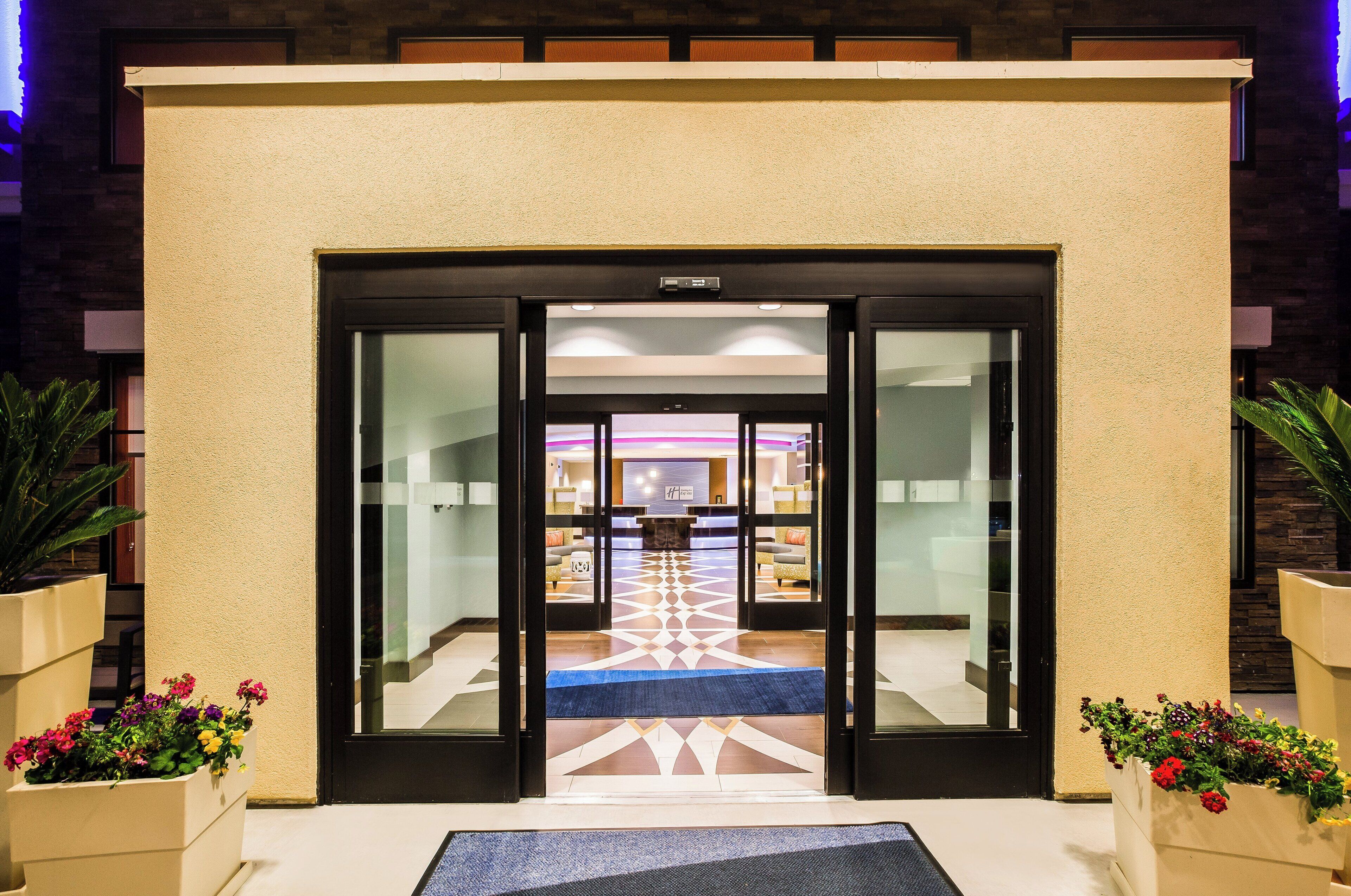 A hotel entrance with a reception desk, a patterned floor, and potted plants.