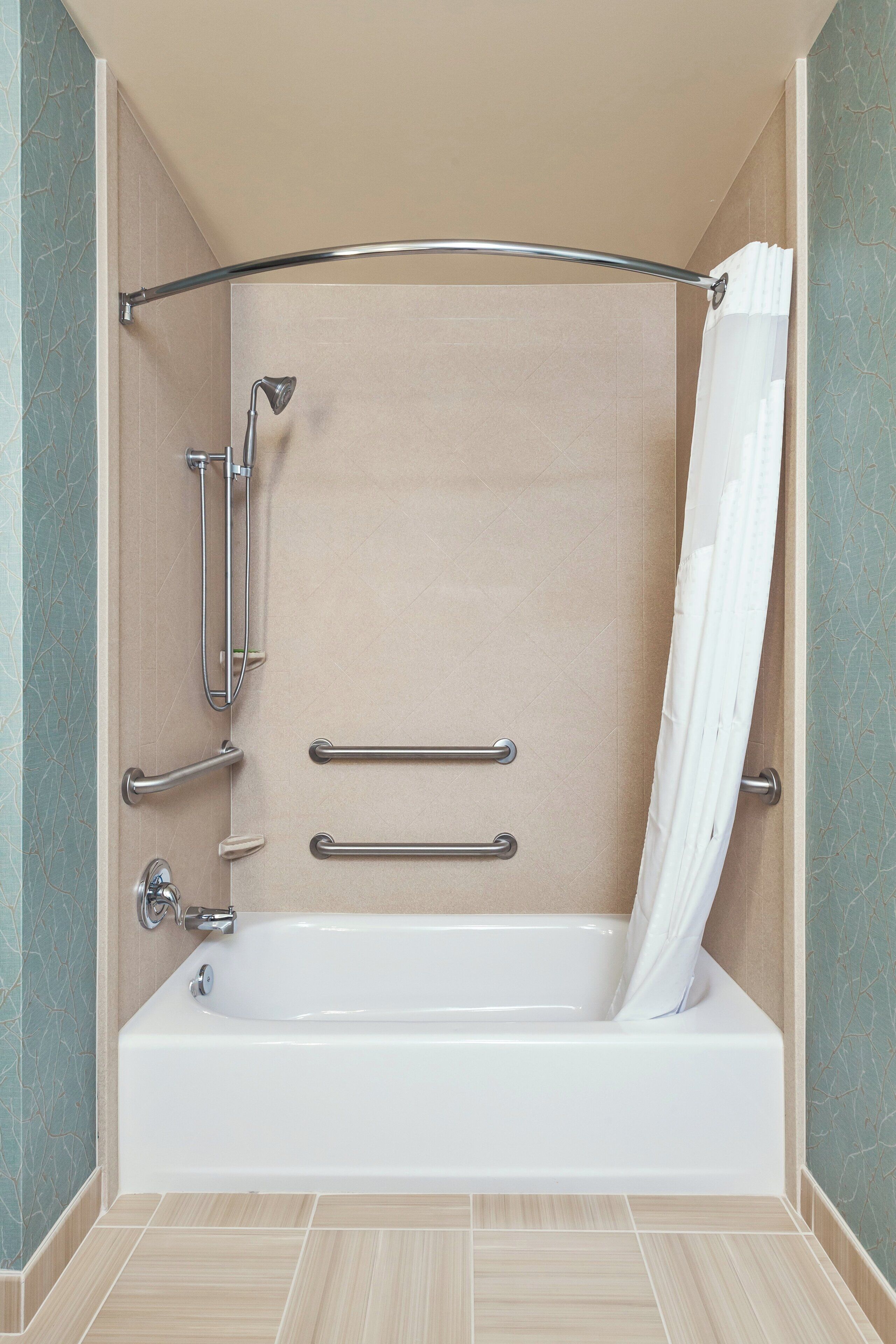 A modern bathroom with a bathtub, grab bars, and a shower head.