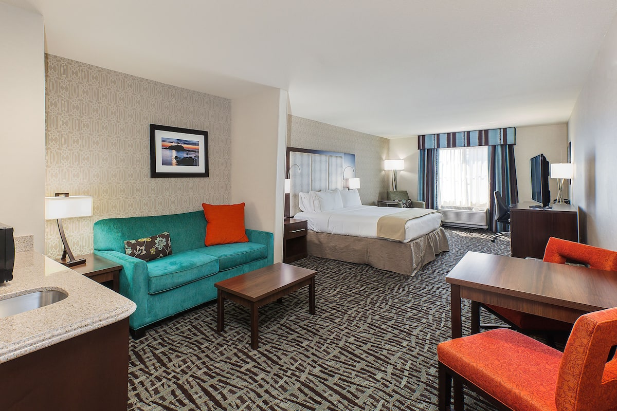 A hotel room with a bed, a sofa, a desk, a chair, a TV, and a bathroom.