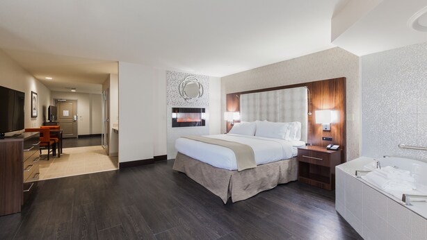 A hotel room with a large bed, a desk, a chair, a TV, a bathroom with a bathtub, and a mirror on the wall.