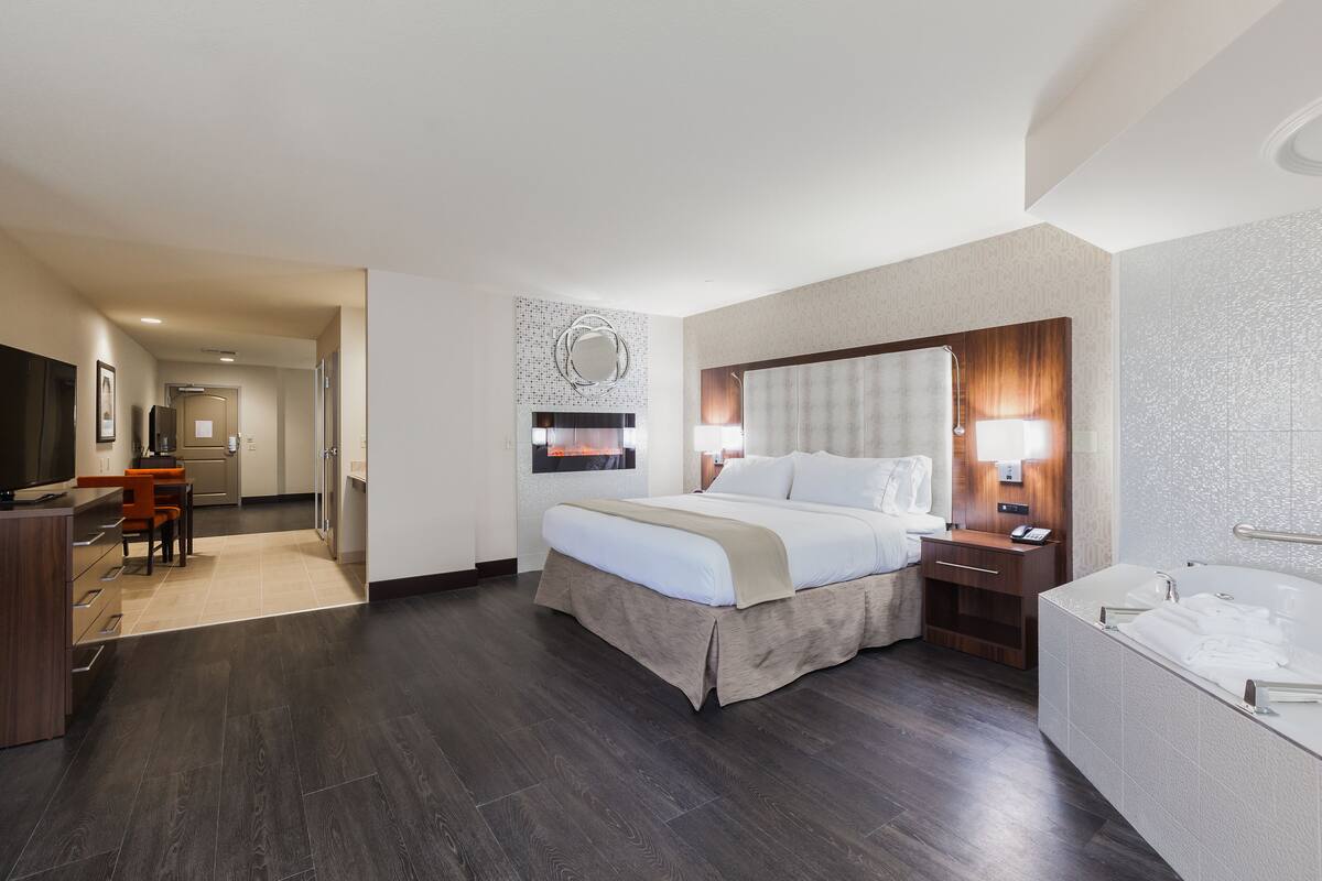 A hotel room with a large bed, a desk, a chair, a TV, a bathroom with a bathtub, and a mirror on the wall.