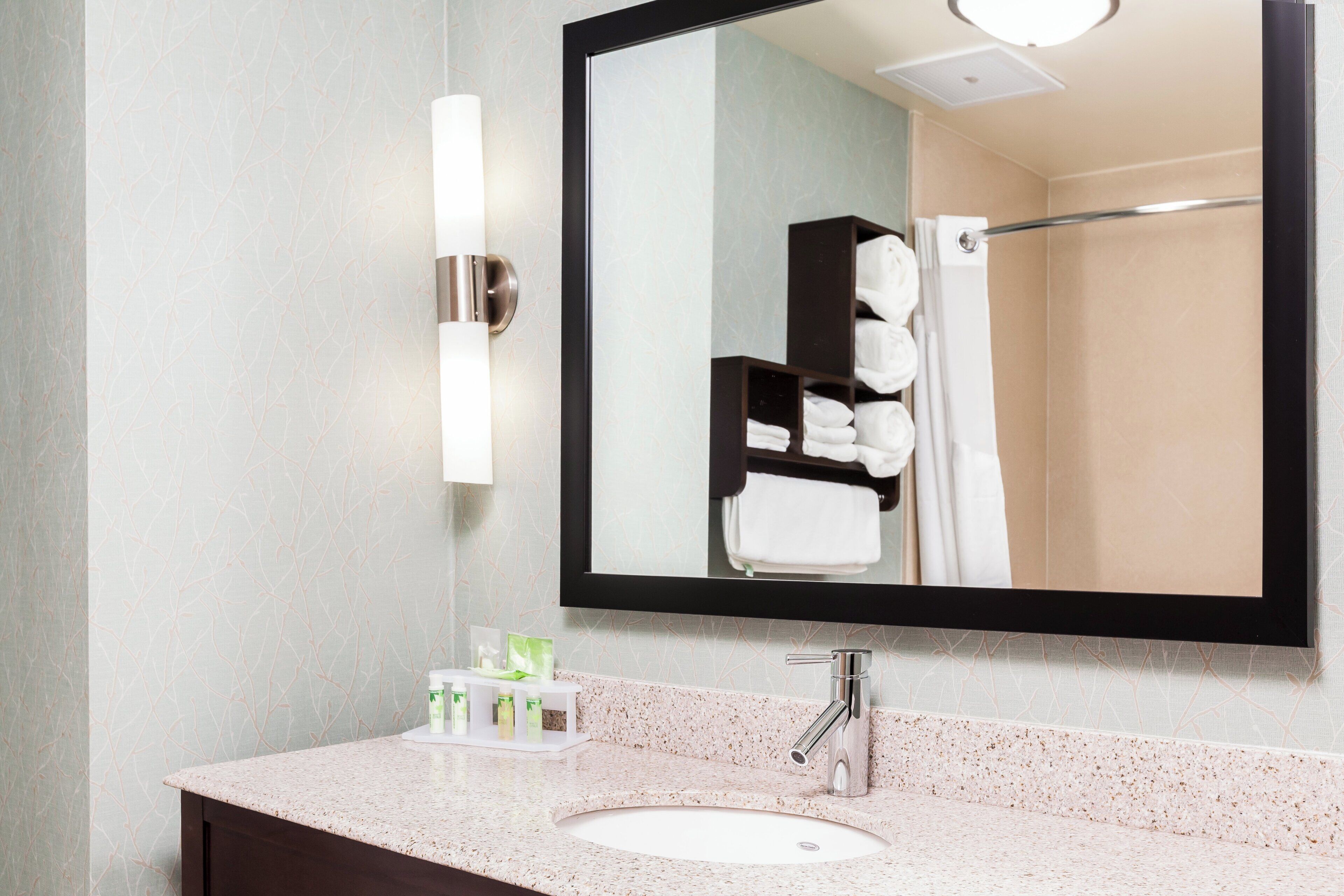 Une salle de bain équipée d’un lavabo, d’un miroir, d’un porte-serviettes et d’articles de toilette.