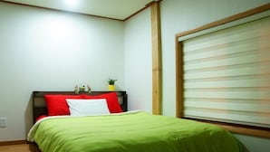 Un dormitorio con cama, ventana con persianas, una planta pequeña en la mesita de noche y un enchufe en la pared.