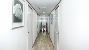 Un pasillo estrecho con suelo de madera, paredes blancas y cuadros en la pared izquierda.