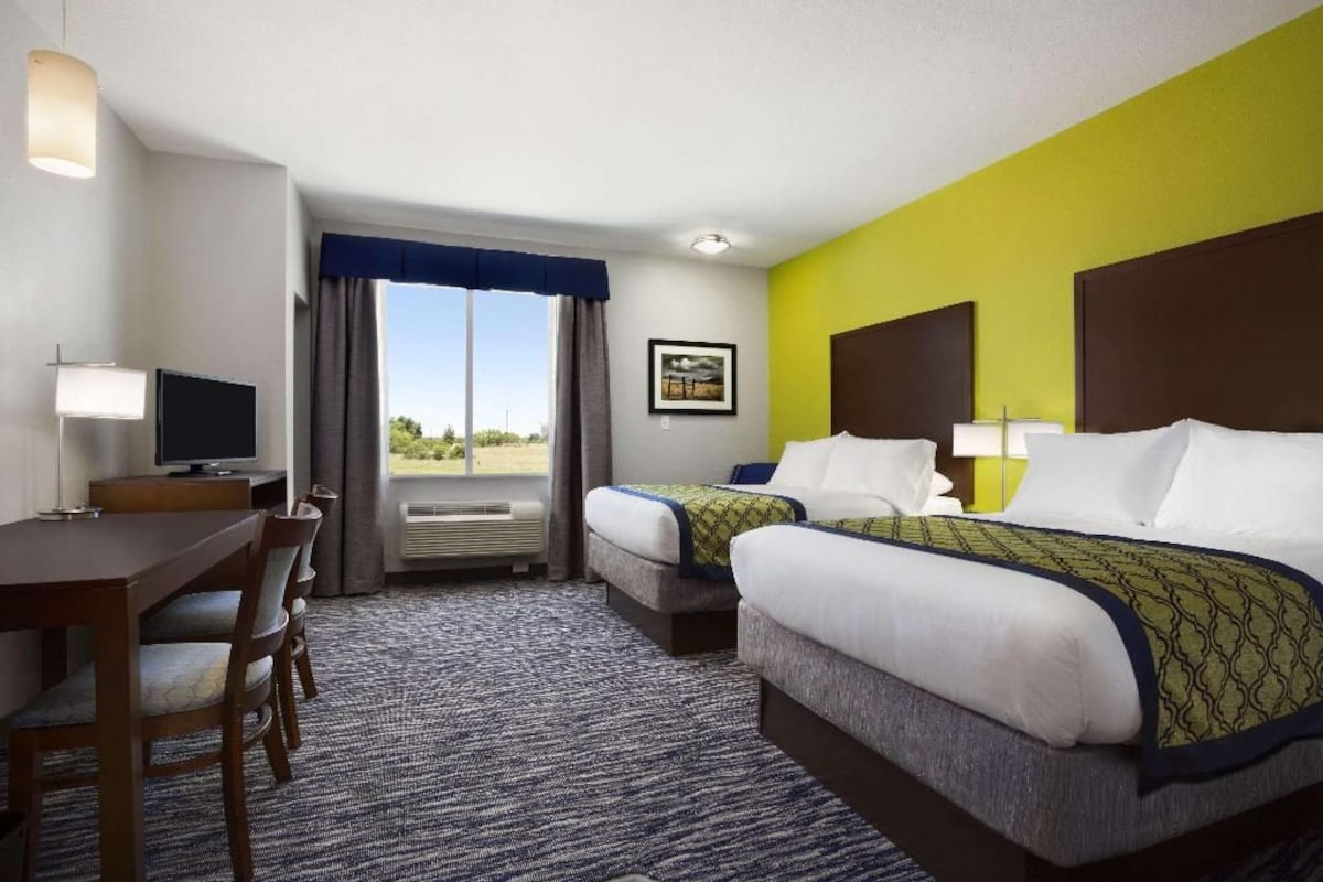 A hotel room with two beds, a desk, a chair, a television, and a window with curtains.