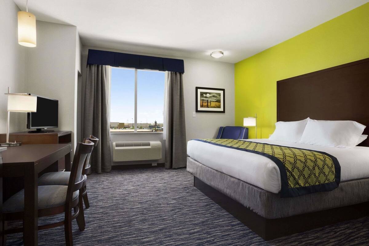 Een hotelkamer met een bed, bureau, stoel, televisie, airconditioning en een raam met gordijnen.