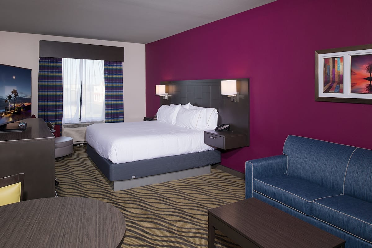 A hotel room with a bed, a desk, a couch, and a nightstand with lamps.