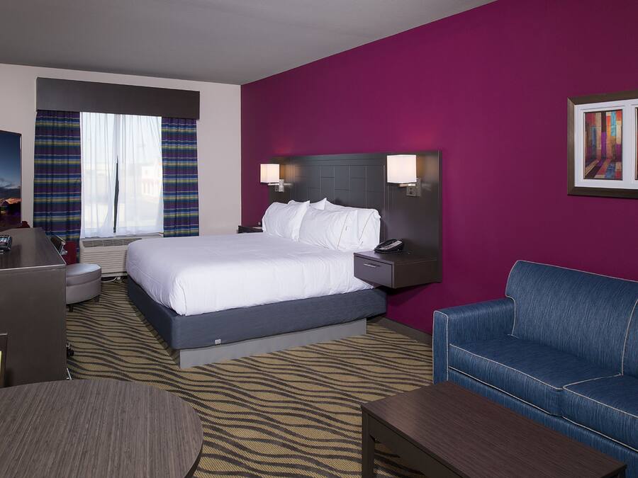 Quarto de hotel com cama, escrivaninha, sofá e mesa de cabeceira com luminárias.