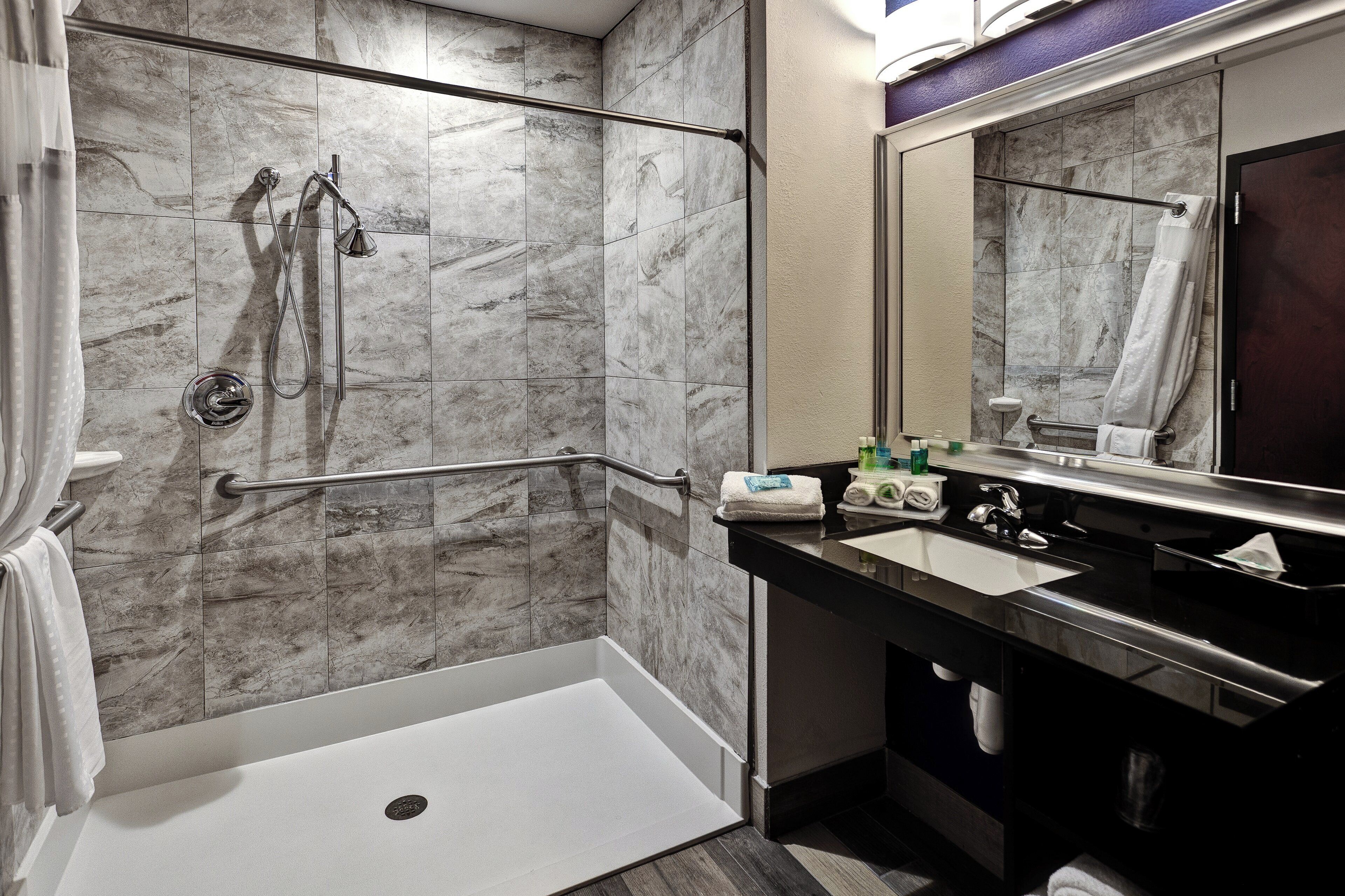 Une salle de bain moderne équipée d’une douche, de barres d’appui, d’un lavabo et d’un miroir.