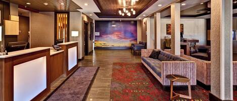 A hotel lobby with a reception desk, seating area, and a mural on the wall.