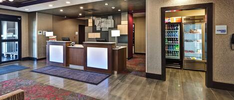 A hotel lobby with a reception desk, a refrigerator with beverages, and a sign for the sundries shop.