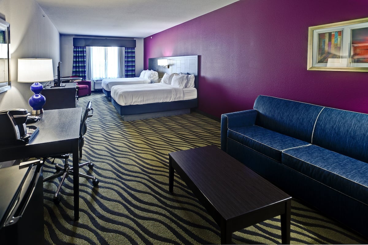 A hotel room with two beds, a desk with a lamp, a blue sofa, and a patterned carpet.