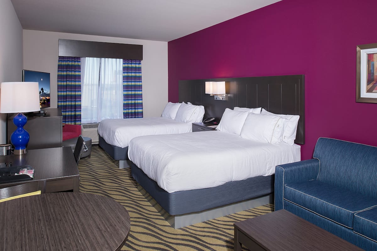A hotel room with two beds, a desk, a chair, and a couch.