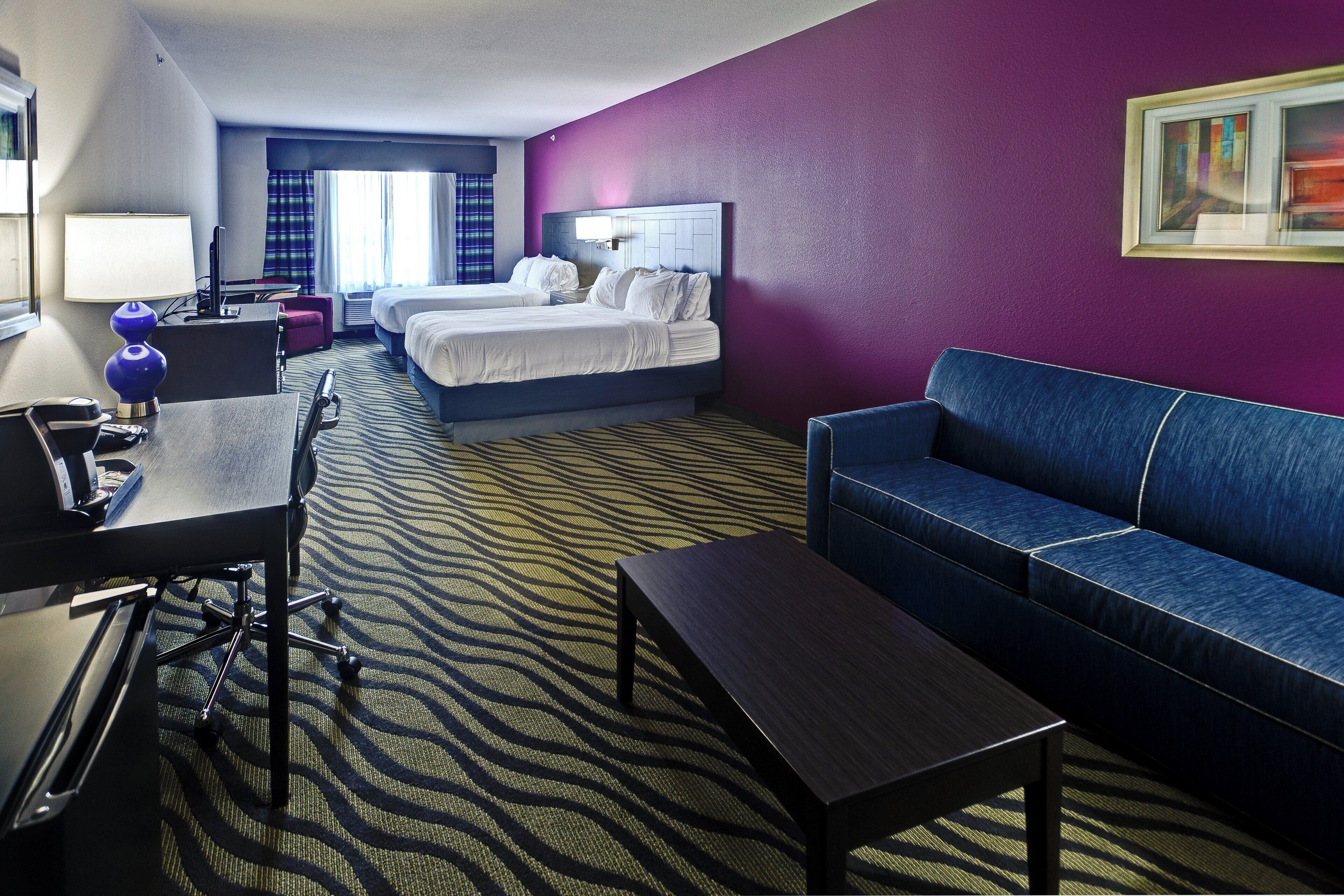A hotel room with a bed, a desk, a chair, a sofa, and a carpet with a geometric pattern.