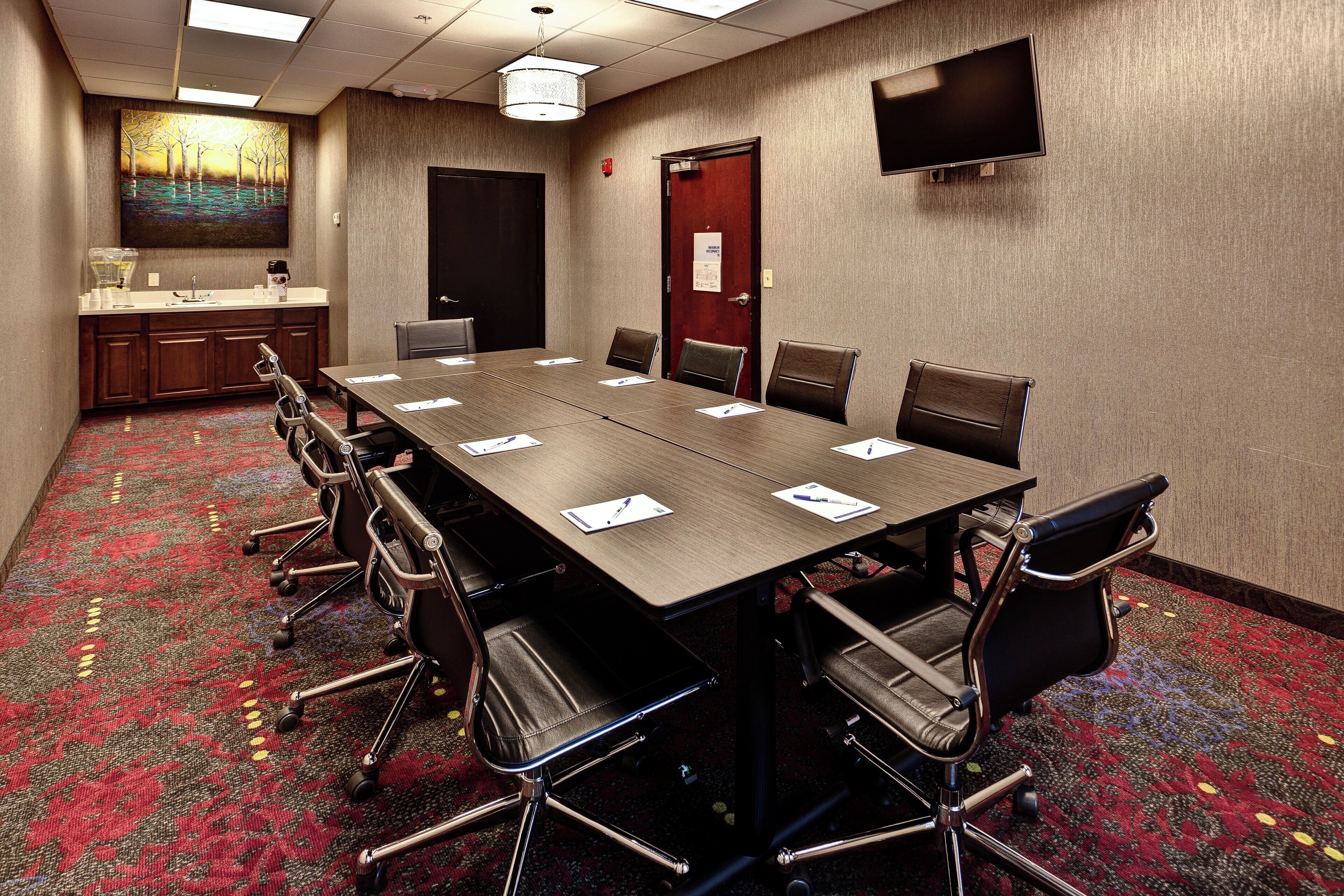 A conference room with a long table, chairs, a television, and a painting on the wall.