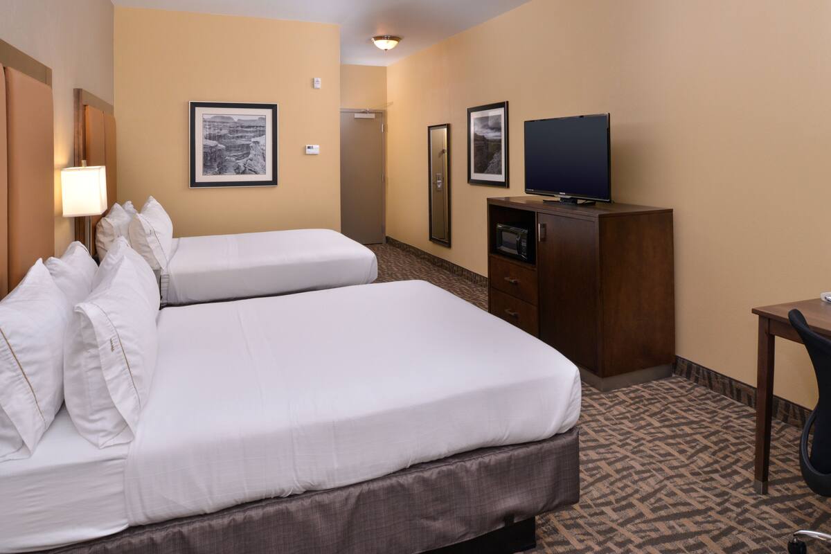 A hotel room with two beds, a television on a cabinet, and framed pictures on the wall.