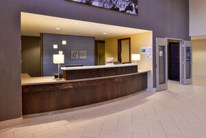 Un mostrador de recepción de hotel con un diseño moderno, una pantalla digital en la parte superior y un cartel con el nombre del hotel.