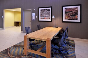 Een vergaderruimte met een houten tafel, stoelen, een lamp en ingelijste foto’s aan de muur.