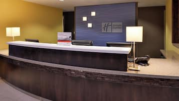 A reception desk with a dark counter, two chairs, a sign for Holiday Inn Express, and a wall with a logo.