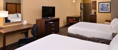 A hotel room with two beds, a desk with a television, a chair, and a small table.