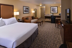 A hotel room with a large bed, a sofa, a desk, a television, and a small kitchenette. - Holiday Inn Express & Suites Page - Lake Powell Area by IHG (Page)