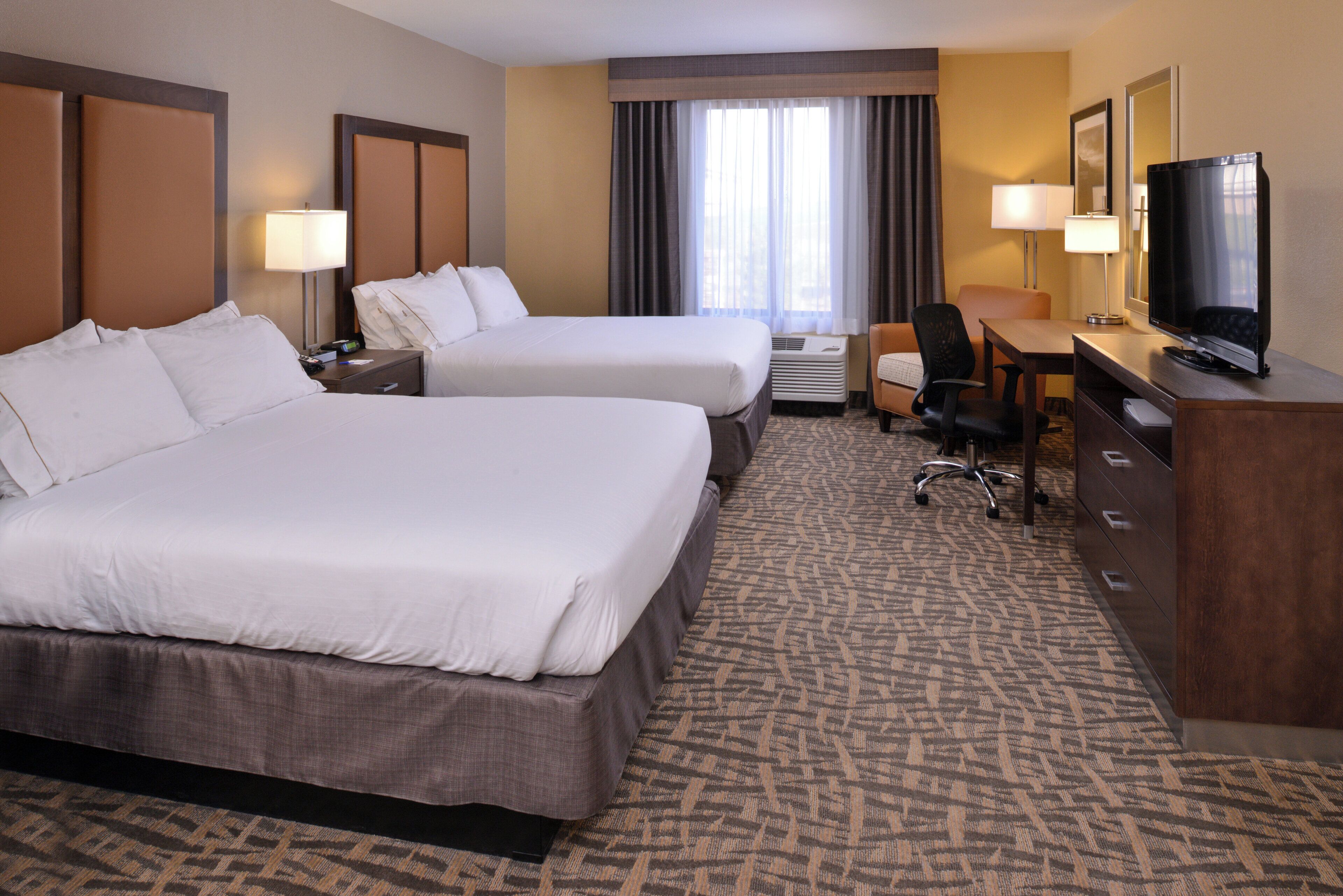 A hotel room with two beds, a desk, a television, and a chair.