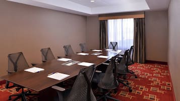 A conference room with a long table, six chairs, and a carpeted floor.