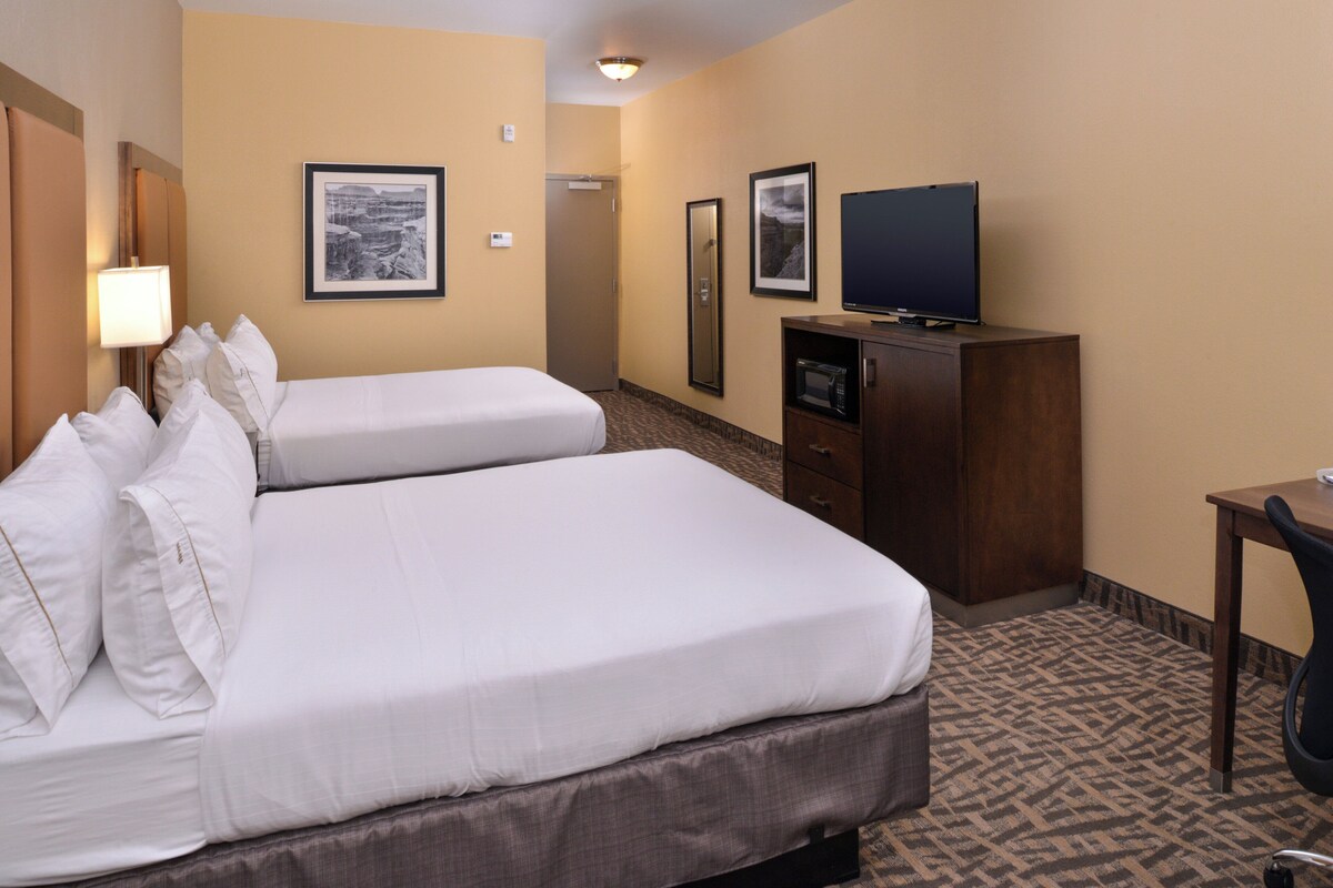 A hotel room with two beds, a television, a desk, and framed pictures on the wall.