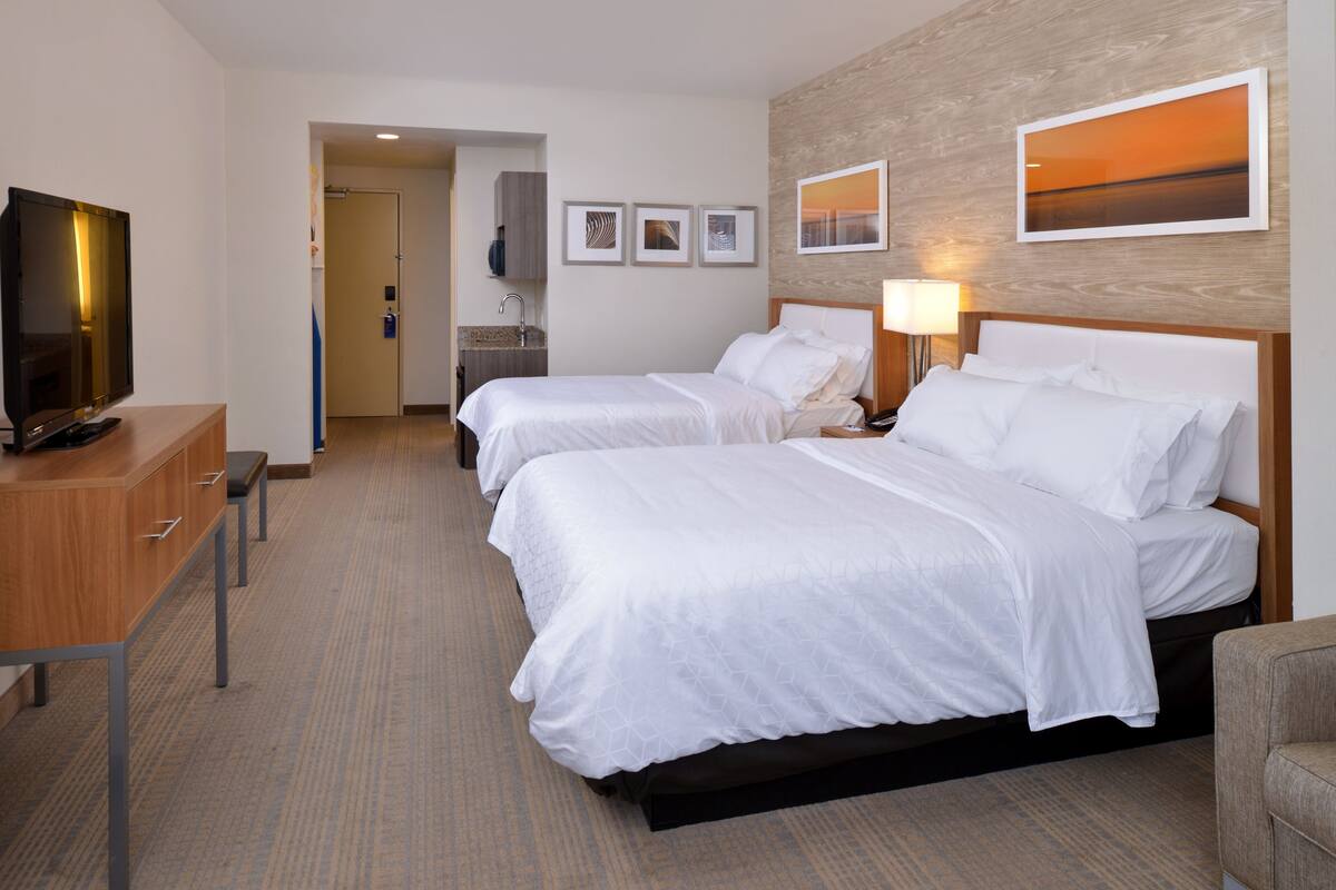 A hotel room with two beds, a TV, a desk, and a bathroom visible through an open door.