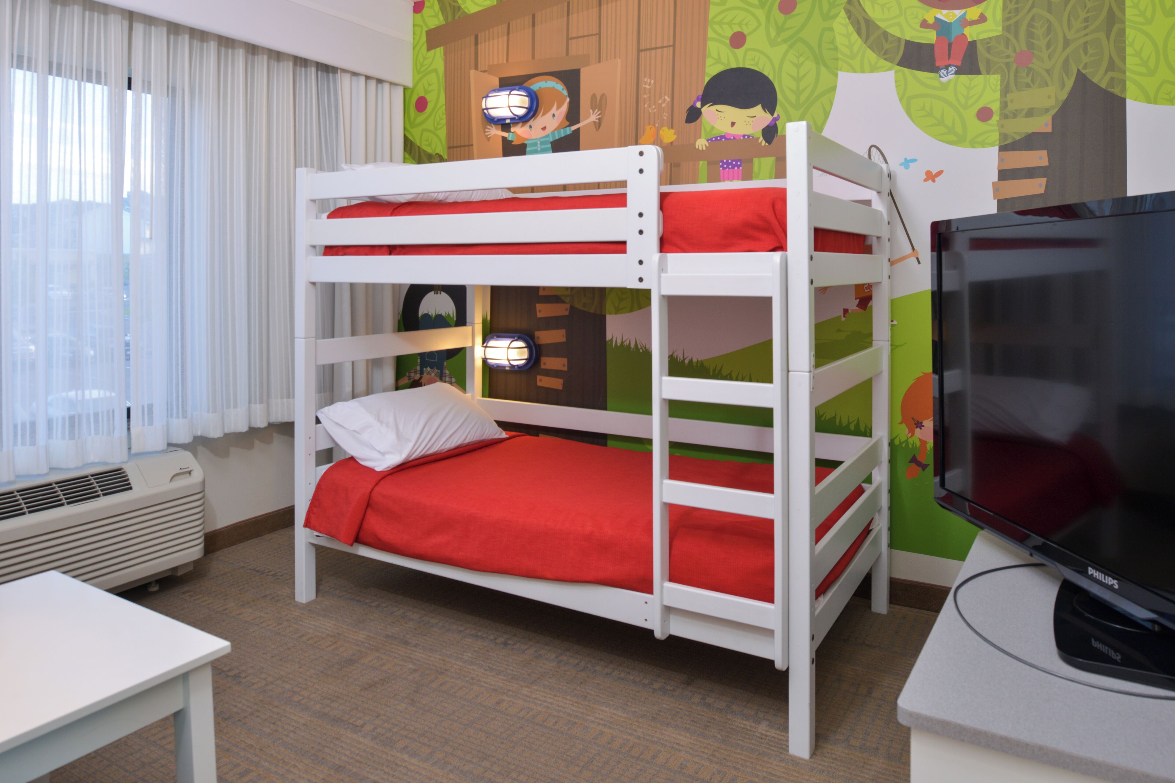 A bunk bed room with a television and a window with curtains.