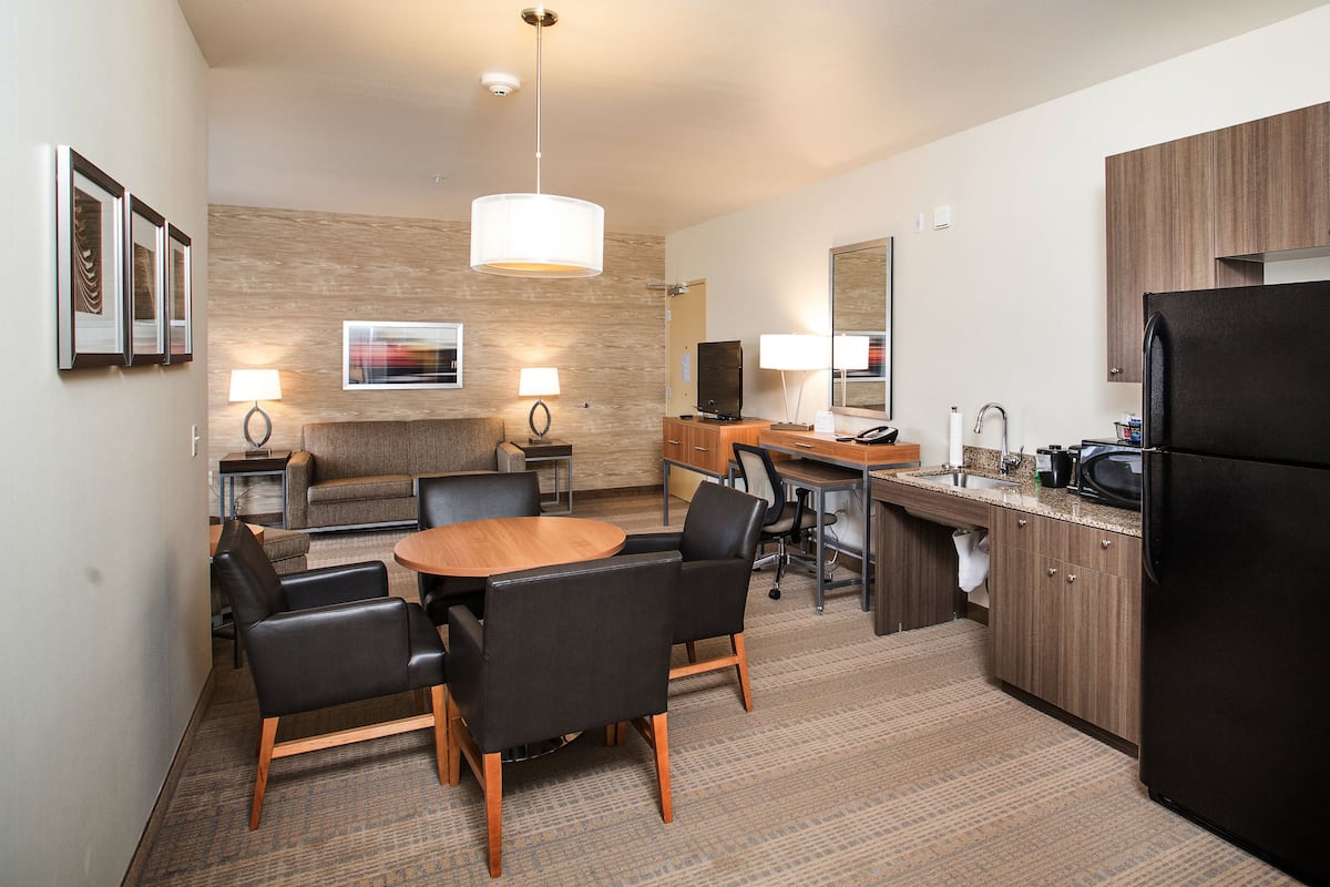 A hotel room with a dining area, a kitchenette, a sofa, and a TV.